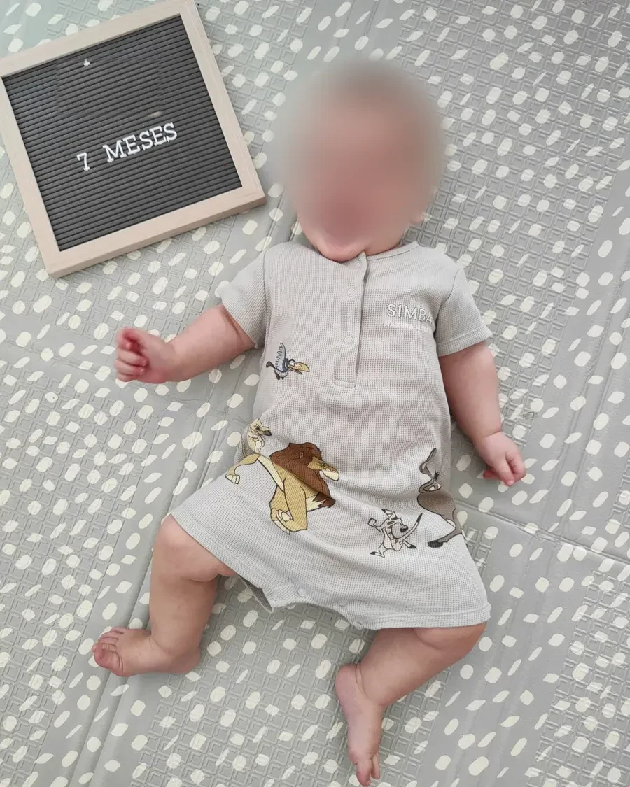 Bebé sonriente tumbado junto a una pizarra que dice 7 meses